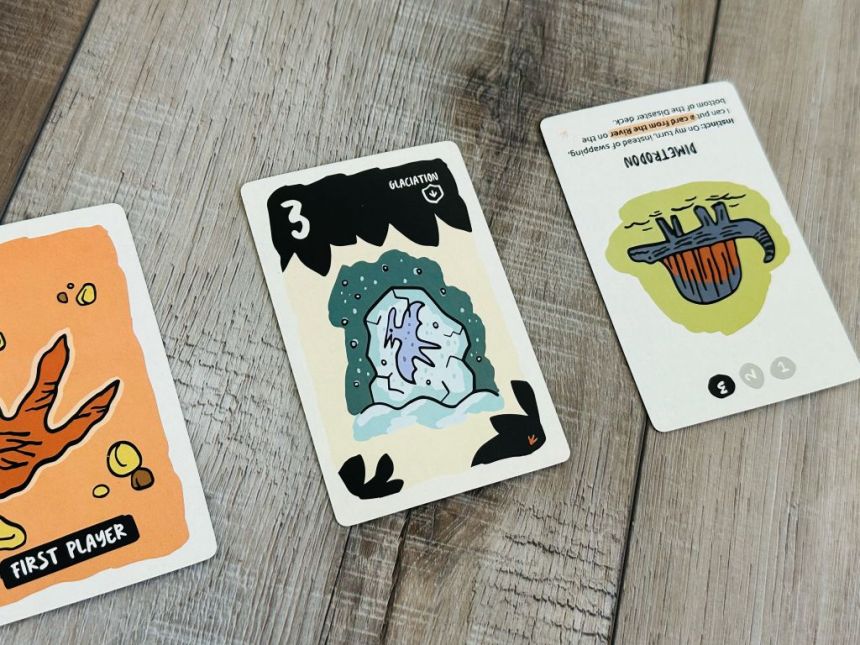 Close up on Very Bad Lands cards: First player, disaster card Glaciation 3, and a Dimetrodon card rotated so the "1" is up.