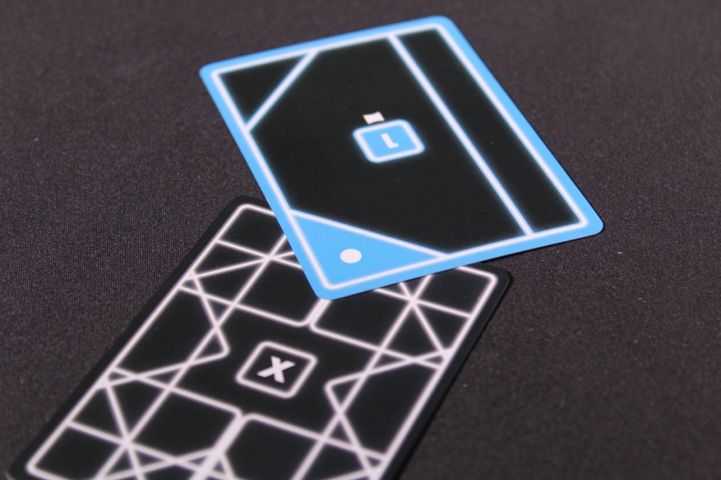 Close-up of two game cards on a dark background, featuring geometric designs and markings for gameplay.