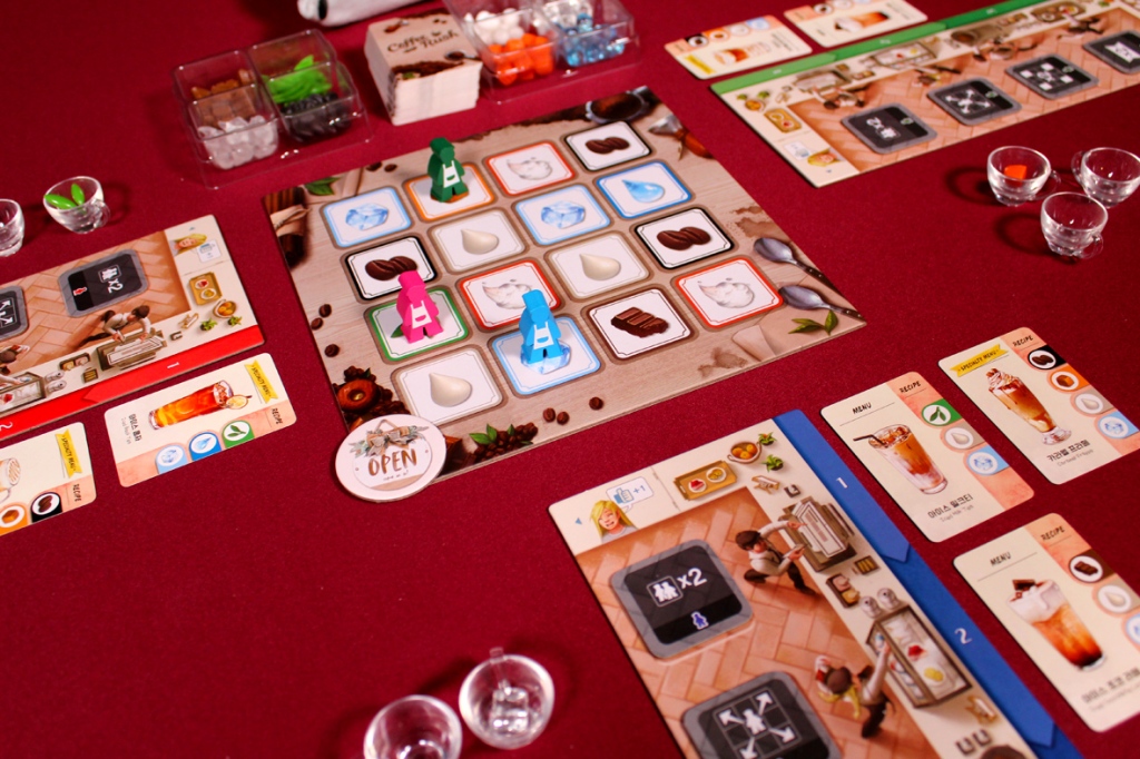 A tabletop game setup for Coffee Rush, featuring player boards, meeples in different colors, ingredient tokens, and order cards arranged on a maroon background.
