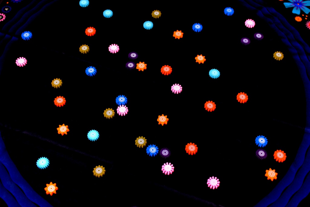A close-up view of colorful flower tokens scattered on a dark surface, with a variety of colors including blue, pink, orange, and yellow.